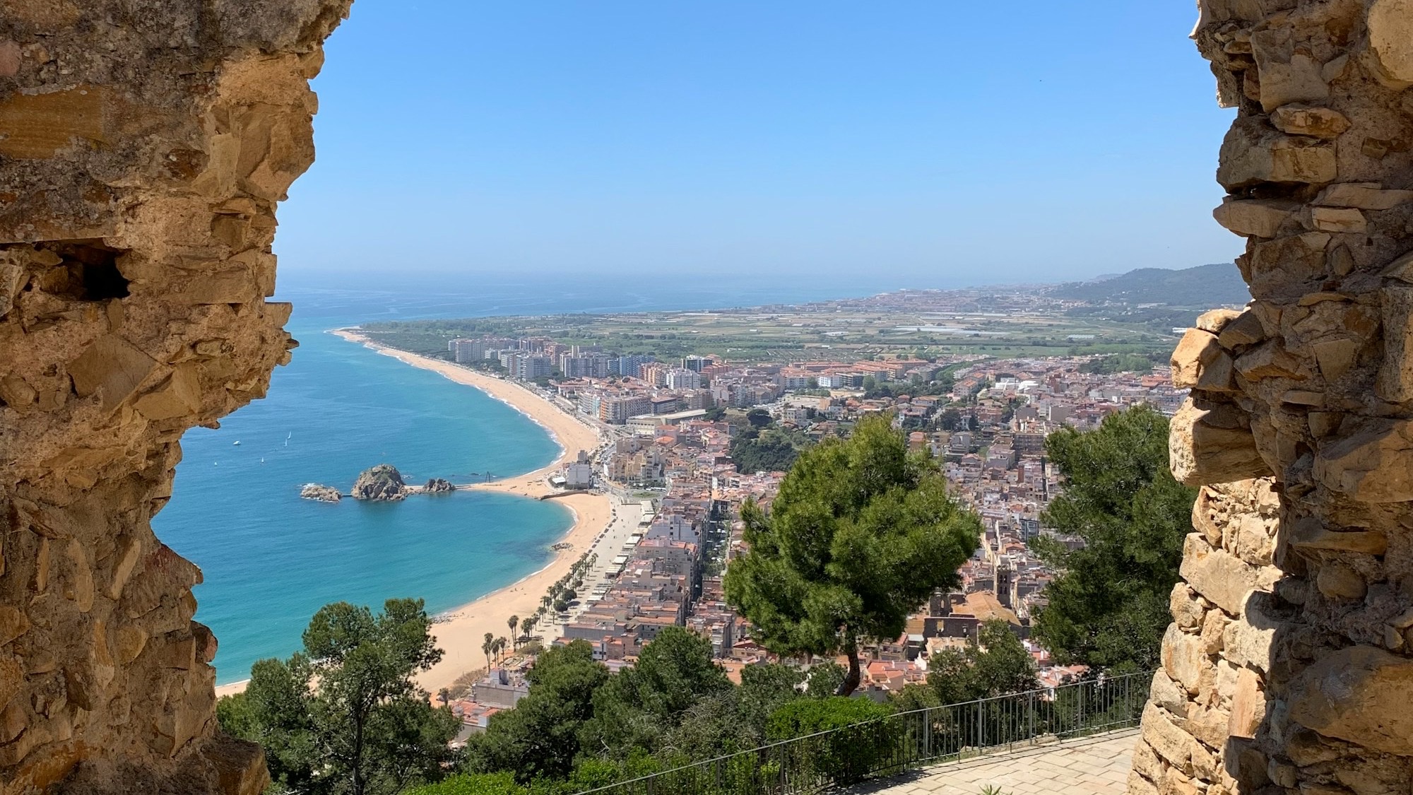 Vista panorámica de la bahía de Blanes desde el Castell de Sant Joan, con Sa Palomera, la playa de S'Abanell y el casco urbano enmarcados por un arco de piedra