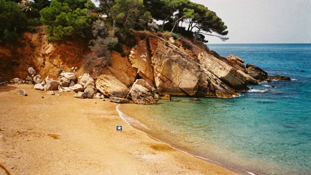 Cala pequeña bandera azul de Blanes con arena dorada, aguas turquesa cristalinas y un acantilado boscoso con pinos mediterráneos en uno de los lados