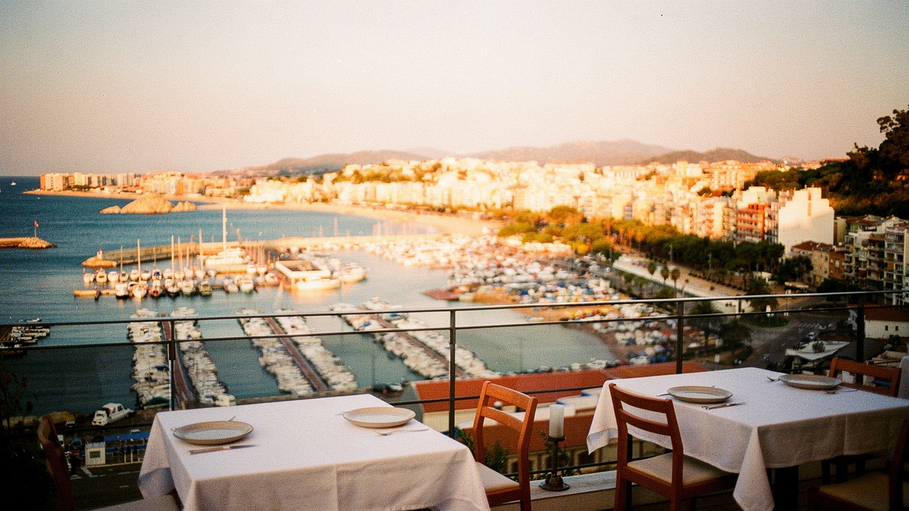 Terraza de restaurante junto al puerto pesquero de Blanes al atardecer con mesas de madera, mantelería blanca y barcas amarradas visibles al fondo a la luz dorada