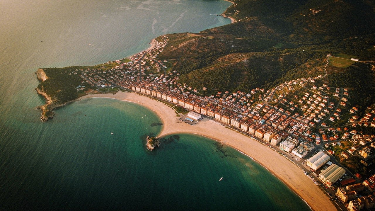 Vue panoramique de Lloret de Mar depuis un belvédère avec la baie en arc, la longue plage, les bâtiments bas et les collines avec pins de part et d'autre au coucher du soleil