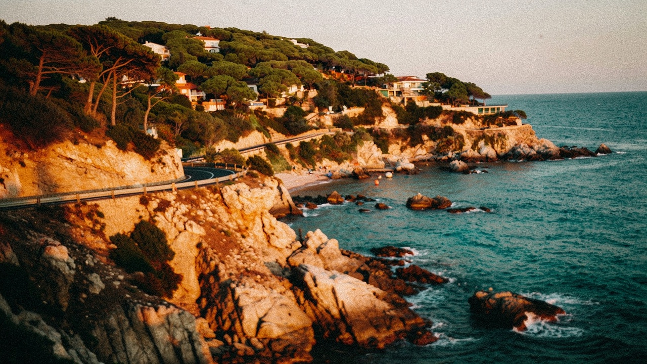 Route côtière avec virages serpentant le long d'une falaise méditerranéenne avec vues sur la mer turquoise et pins couvrant les pentes à la lumière dorée
